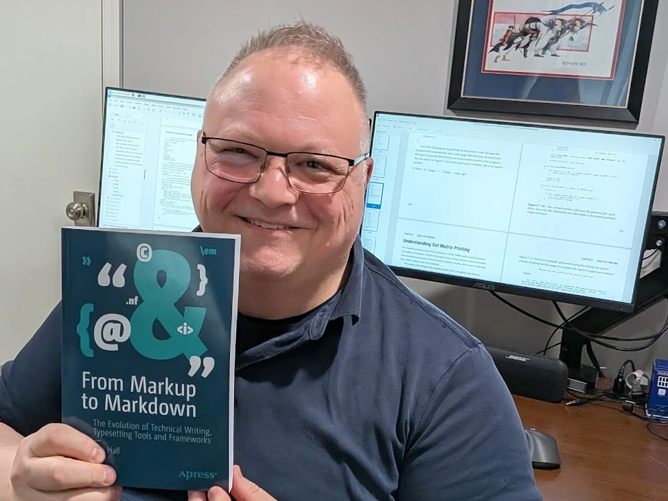 a smiling man holds a copy of a book, with a blue cover and white text